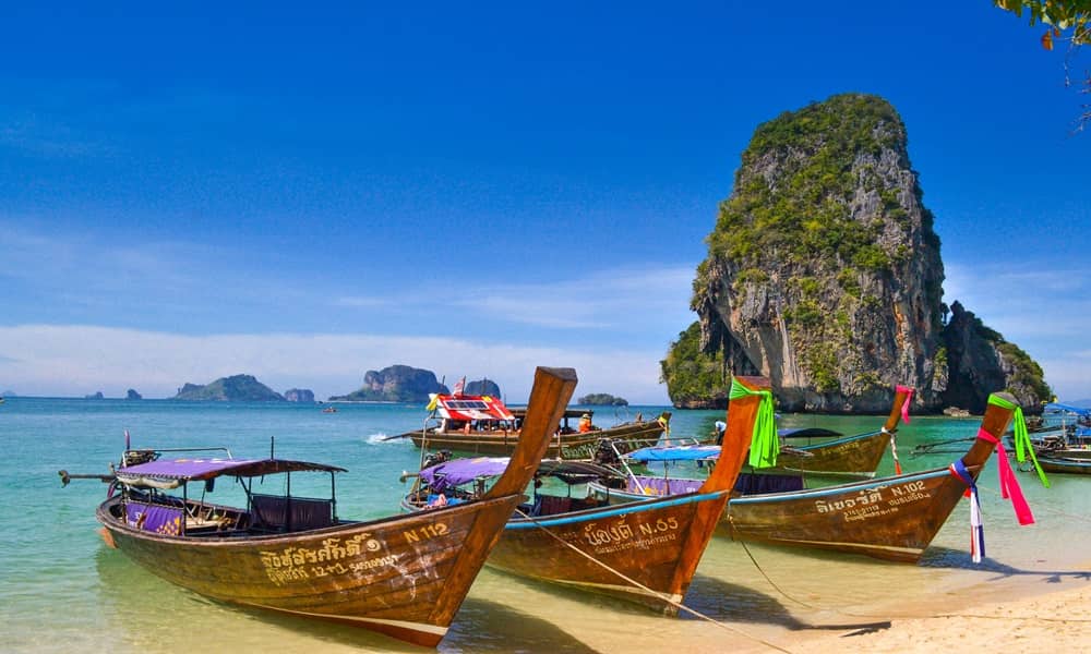 Três barcos tradicionais da Tailândia ancorados na praia de Railay Beach