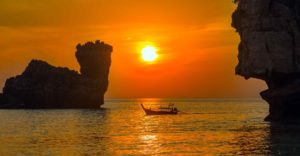 Pôr do sol com um long tail distante nas águas da praia de Nuy Bay em Phi Phi