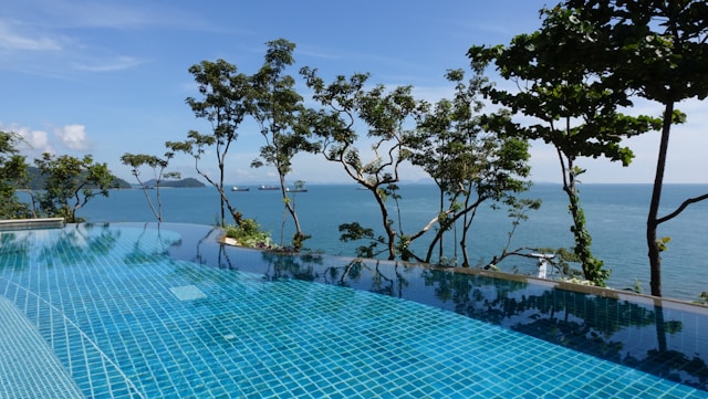 Piscina de borda infinita com vista para o mar e árvores ao redor, em um dia ensolarado na Tailândia. | Phi Phi Brazuca