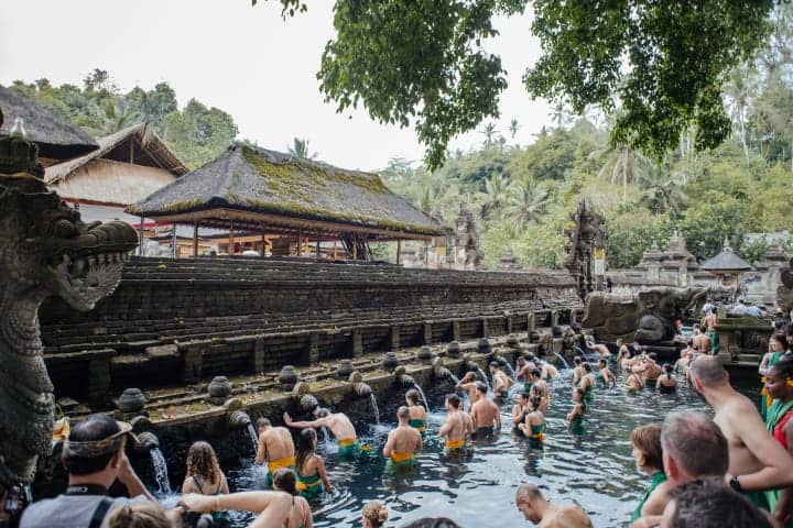 Perto do mar em Bali, turistas aproveitam banho nas fontes sagradas de Tanah Lot, um dos principais pontos turísticos culturais e religiosos.