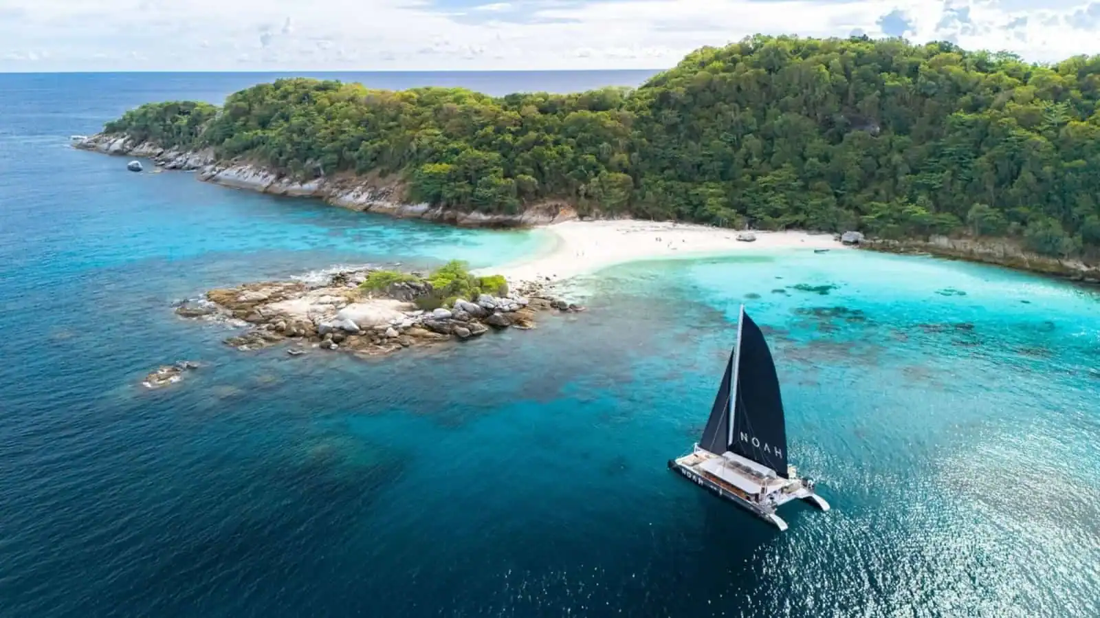 Praia de Phi Phi com águas cristalinas, ilha verdejante e barco de vela navegando na costa.