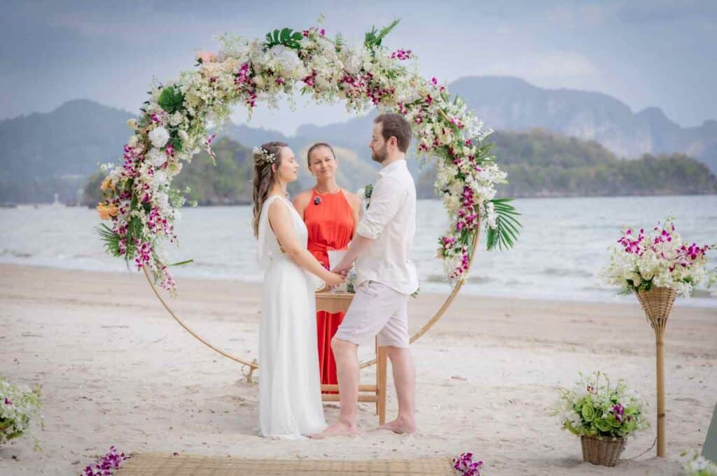 Arco de flores para casamento na praia com noivos e celebrante.