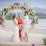 Arco de flores para casamento na praia com noivos e celebrante.
