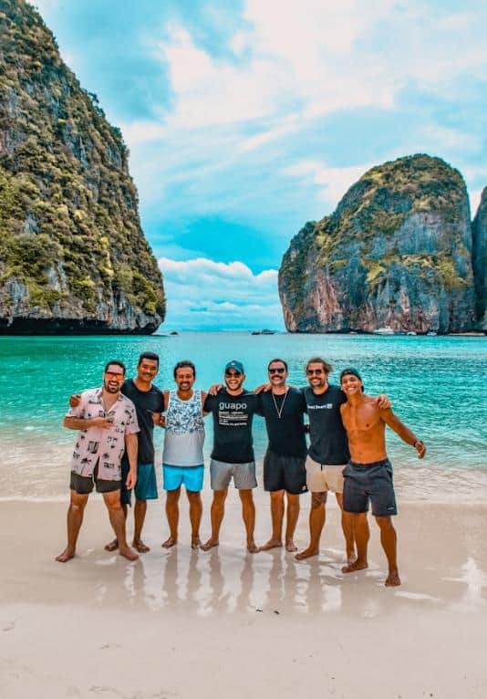 Viagem em grupo na praia de Phi Phi, Tailândia, com vista para o mar cristalino e formações rochosas.