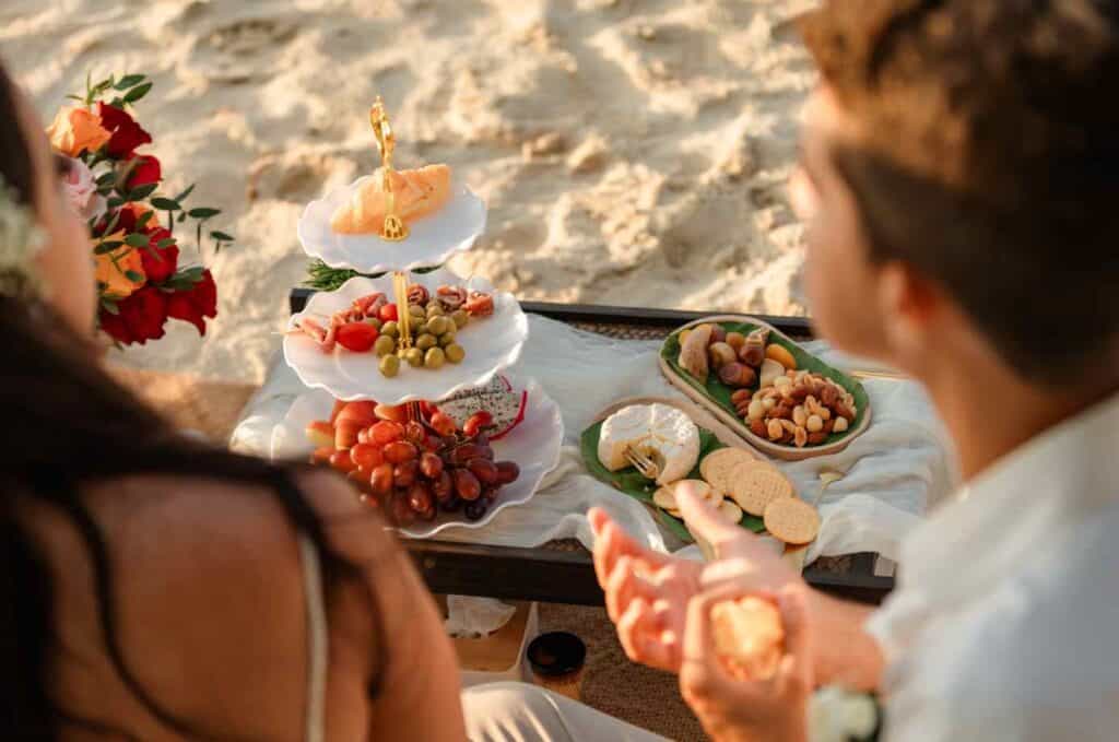Mesa de doces e frutas na praia para casamento ao pôr do sol.