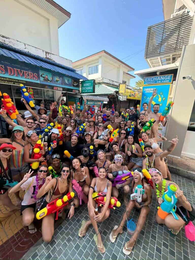 Diversão em grupo na praia de Phi Phi Brazuca, com pessoas usando fantasias e brinquedos aquáticos.