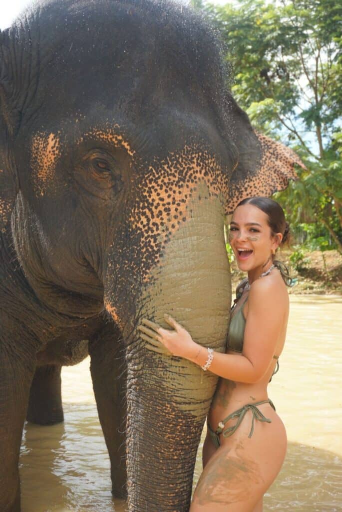 Elefante e mulher sorridente na água, interagindo em ambiente natural tropical.